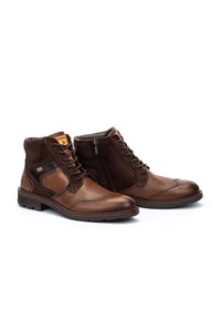 Stivali alla caviglia in pelle e suede marrone con lacci e cerniera laterale, caratterizzati da motivi testurizzati e materiali a contrasto.