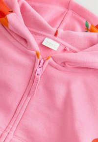 Rosa Kapuzensweatshirt mit einem Frontreißverschluss und orangen floralen Akzenten. Weicher Stoff mit glatter Textur. Markenlabel innen sichtbar.