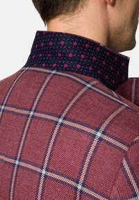 Czerwona kraciasta koszula z teksturowanym splotem, z granatowym kołnierzykiem w różowe kropki i motywy koron. Wyraźne detale przeszycia.