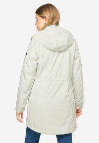 Kevyt, hupullinen parka vaaleanharmaana. Ominaisuuksina kireä vyötärö ja ribattu hihansuu, jossa hienovaraiset ompeluyksityiskohdat. Sujuva pinta, polveen ulottuva leikkaus.