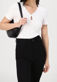 Top blanco de manga corta con detalle de ojal, combinado con jeans negros de cintura alta y un bolso negro con tachuelas.