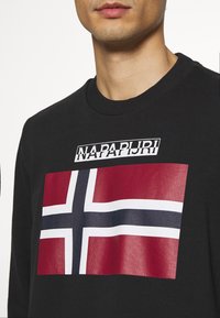 Sudadera negra con un gráfico de la bandera de Noruega en rojo, blanco y azul, con el texto "NAPAPIJRI" encima de la bandera en una fuente en negrita.