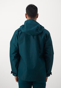 Dark teal waterproof jacket with a hood, featuring a relaxed fit, adjustable cuffs, and a smooth, matte texture. Back view shown.
