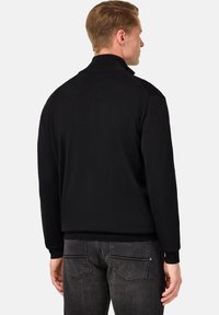 Mustmustega, kõrge kaeluse, soonikkääride ja lõhiku äärtega. Sile tekstuur ühtlase värviga. Kantud tumedate hallide teksadega.