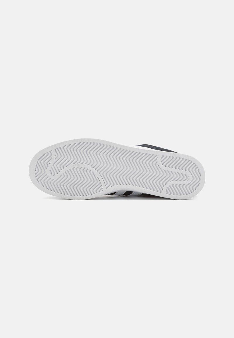 Suela de zapato deportivo negra con una suela de goma blanca que presenta un patrón en zigzag. Textura duradera con líneas curvas para mayor agarre.