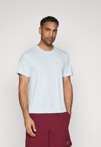 Ανοιχτό μπλε αθλητικό μπλουζάκι φτιαγμένο από απαλό ύφασμα, με κοντά μανίκια, στρογγυλή λαιμόκοψη και μια μικρή ετικέτα στην αριστερή πλευρά.