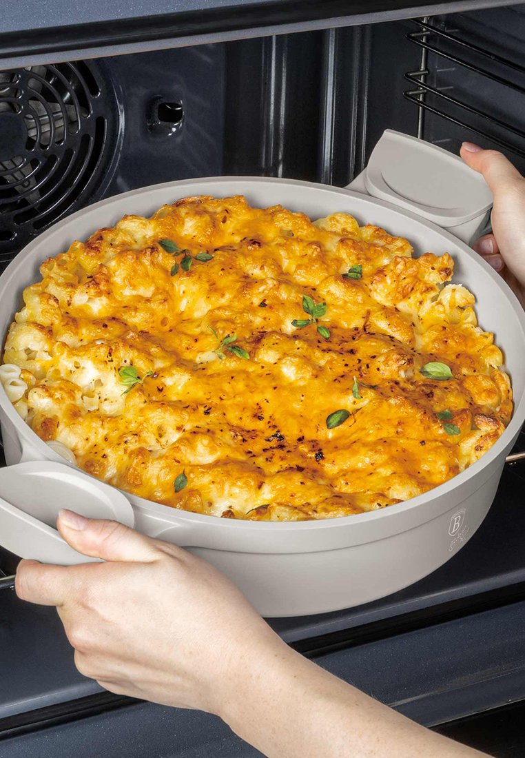 Des mains retirant un plat rond de macaroni au fromage cuit, avec du fromage fondu et une garniture d'herbes, du four.