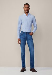 Camisa de botones azul clara y jeans azules oscuros. La camisa tiene cuello y está hecha de una tela suave; los jeans son ajustados y tienen un diseño minimalista.
