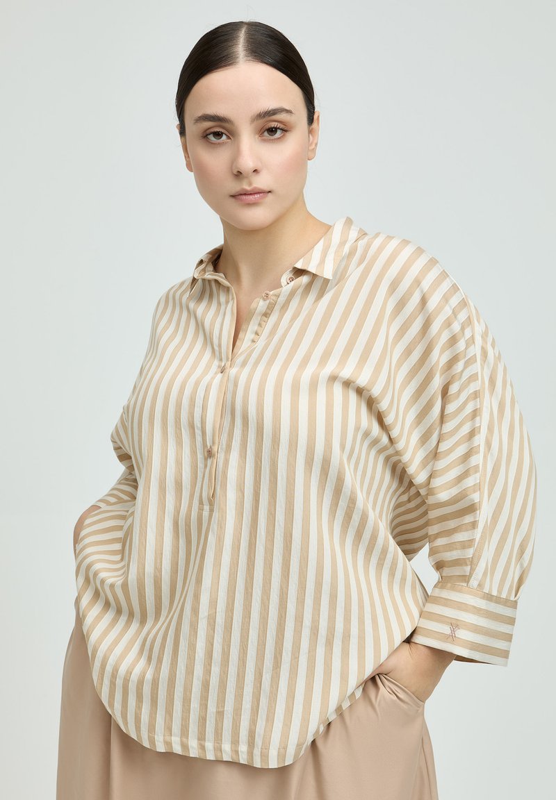 Beige and cream striped button-up shirt with a collar, long sleeves, and loose fit; features subtle cuff detail and textured fabric.
