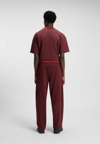 Maroon tracksuit consisting of a short-sleeve top with a red trim and loose-fitting pants. Smooth fabric with a subtle sheen. Black footwear.