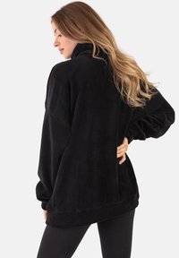 Czarny polarowy sweter z wysokim kołnierzem, w luźnym kroju i długimi, puszystymi rękawami. Posiada subtelną teksturę oraz detale na bocznych szwach.