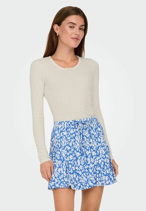 Haut à manches longues côtelé beige clair associé à une jupe courte à motif floral bleu, dotée d'un cordon de serrage et d'une texture plissée.