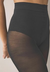 Colanți negri cu talie înaltă, textură mată netedă și secțiuni semi-transparente, având o talie fără cusături și un croi mulat.