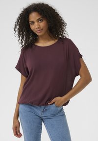Burgunderfarbenes T-Shirt mit kurzen Ärmeln und Rundhalsausschnitt, in legerem Schnitt, kombiniert mit hellblauen, figurbetonten Jeans. Weicher Stoff mit feiner Textur.