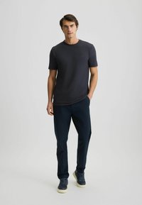 Dunkelgraues T-Shirt mit kurzen Ärmeln und rundem Halsausschnitt. Kombiniert mit navyblauen Hosen und navyblauen Sneakers. Glattes Material und dezentes Logo-Detail.