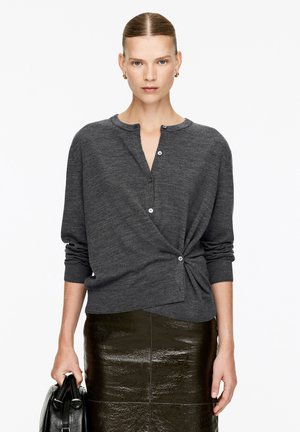 Gray button-up cardigan with a round neckline, textured fabric, and twisted detail at the waist, paired with a glossy dark skirt.