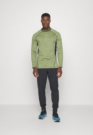 Maglietta verde a maniche lunghe con tessuto testurizzato, pannelli laterali scuri e scollatura rotonda. Abbinata a pantaloni neri a sigaretta e scarpe da ginnastica nere/blue.