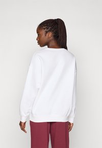 Hanorac alb cu croială lejeră, cu manșete nervurate și decolteu rotund, purtat cu pantaloni de trening vișinii. Textură netedă, design simplu.