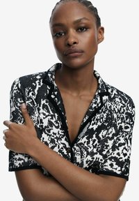 Short-sleeve black and white patterned shirt features a button-up front, notched collar, and contrasting black trim along the edges.