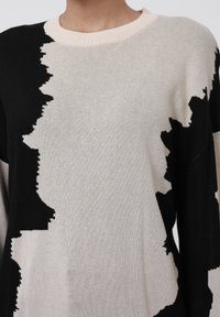 Suéter de punto con un patrón abstracto en negro y crema, con un cuello acanalado y tela texturizada. Corte holgado y mangas largas.