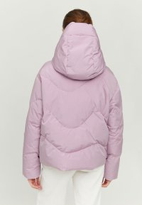 Lilac puffer jacket with a large hood, featuring quilted pattern and a relaxed fit, shown from the back on a person wearing white pants.
