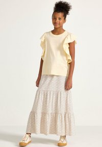 Lys gul, rynket kortærmet top parret med en lang, hvid nederdel med små blomstertryk og lagdelt kant, båret med beige sneakers.