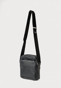 Fekete oldaltáska sima bőrből, cipzárral záródik, állítható pánttal, amelyen dombornyomott márkajelzés található, valamint elülső zsebbel.