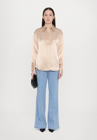 Satin beige shirt with a button-up design, long sleeves, and a smooth texture, paired with light blue flared jeans and a black clutch.