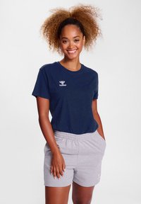 Navy short-sleeve t-shirt with a white logo, paired with light gray elastic waistband shorts featuring side pockets. Smooth, casual fabric.