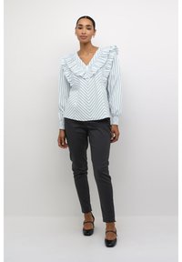 Jasnoniebieska bluzka w pionowe paski z falbanowym dekoltem w kształcie litery V, w zestawieniu z ciemnoszarymi spodniami typu slim fit i czarnymi balerinami.