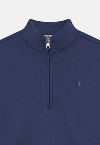 Pullover blu navy con collo alto, chiusura a mezza zip e un piccolo logo sul lato sinistro del petto. Realizzato in un tessuto morbido e testurizzato.