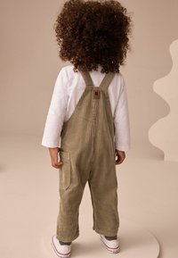 Salopette en velours côtelé vert olive avec des rayures verticales, dotée de bretelles ajustables, d'une poche arrière et d'une chemise blanche à manches longues avec des manches à motifs.