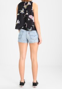 Musta kukkakuosiset hihattomat yläosat, joissa on valuvia muotoja, yhdistettynä vaaleansinihin farkkushortseihin. Rakenneviimeistely, revitty helma ja mustat lenkkarit.