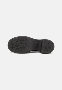 Black rubber shoe sole with geometric tread pattern, rounded shape, and a textured finish; features a small logo in the center.