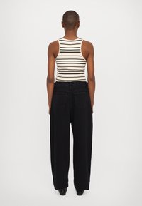 Top de tirantes finos beige a rayas, combinado con pantalones vaqueros anchos de tiro alto en negro. Textura suave, diseño minimalista y sin herrajes visibles.