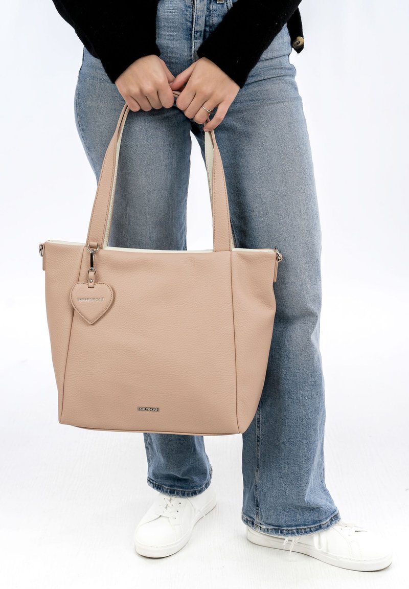 Beige kožená taška přes rameno se strukturovaným designem, vybavená dvěma uchy a přívěskem ve tvaru srdce, na světlém pozadí.