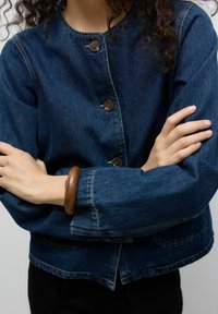 Denim jack in donkerblauw met lange mouwen, ronde hals, knopen aan de voorkant en een cropped ontwerp. Beschikt over zichtbare naden en een relaxte pasvorm.