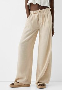 Beige wijde pantalon gemaakt van lichtgewicht stof met een getextureerde afwerking. Voorzien van een elastische tailleband en een trekkoord, ontworpen voor comfort.