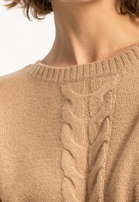 Khaki sweter z dzianiny z prążkowanym dekoltem i wyraźnym wzorem w warkocze na środku. Miękka, teksturowana tkanina o przytulnym wyglądzie.
