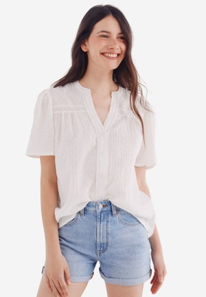 Witte blouse met korte mouwen en een knoopsluiting aan de voorkant, van textuurstof met kantaccenten, gecombineerd met lichtdenim shorts.