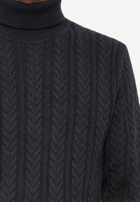 Tamsiai pilkas megztas turtleneck megztinis, kuriame yra tekstūruotas kabelių raštas su iškiliais siūlais ir aukštu kaklu.