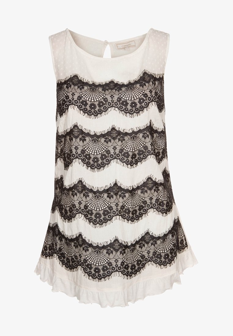 Mouwloos topje van witte stof met een gestructureerde afwerking, voorzien van zwarte kantdetails in golvende patronen en een gerimpelde zoom. Sleutelgatrug.