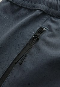 Voděodolná tmavě šedá tkanina s texturovaným povrchem, obsahující kapsu na zip s černými prvky a kapky deště na materiálu.