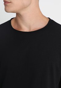 Musta crew-neck t-paita, jossa on pehmeä, tekstuuriainen kangas ja rento istuvuus, sekä minimaalisesti saumoja näkyvissä kaula-aukon ympärillä.