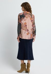 Multicolored blouse with paisley and geometric patterns, long black sleeves, and a curved hem. Paired with a dark denim skirt and tan boots.