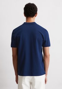 Tmavě modrá polo košile s krátkými rukávy a klasickým límečkem. Hladká textury, boční rozparky na lemu a minimální detaily švů.