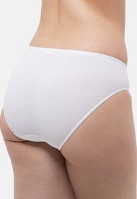 Slip bikini bianco in cotone con una texture liscia, fascia elastica e taglio classico, mostrato da dietro in un contesto neutro.