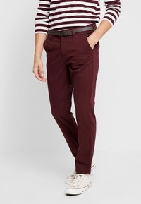 Mörk röda slim-fit chinos med en flat frontdesign, med sidofickor och ett brunt bälte, matchade med vita sneakers och en randig skjorta.