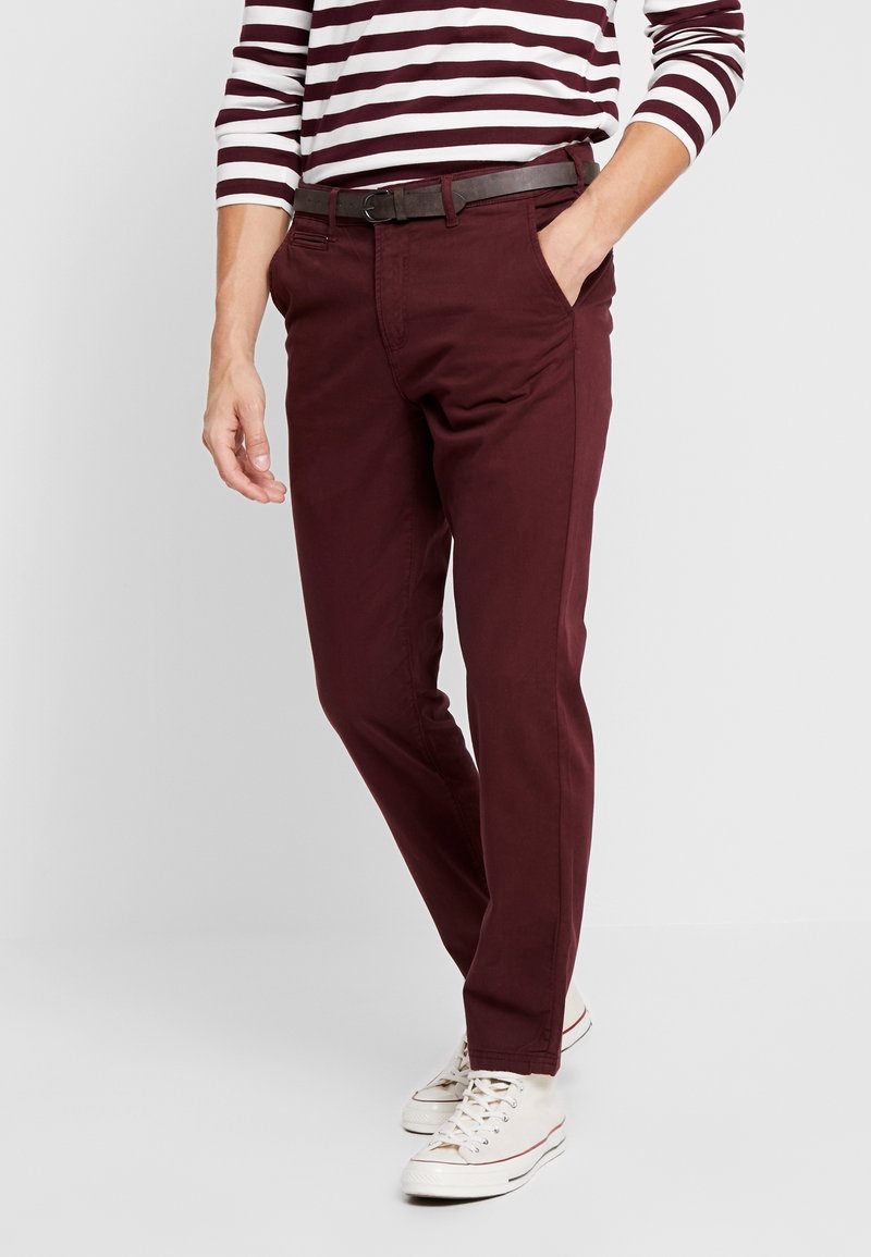 Mörk röda slim-fit chinos med en flat frontdesign, med sidofickor och ett brunt bälte, matchade med vita sneakers och en randig skjorta.