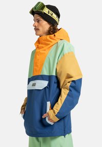 Bunter Anorak-Jacke mit orangefarbenen, grünen und blauen Paneelen; lockere Passform; Kapuze; Fronttasche; aus wasserabweisendem Material.